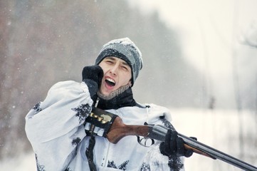 Man (hunter) in winter camouflage hit the butt of a gun in the chin from the recoil when fired