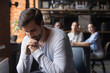 © fizkes - Sad guy sitting alone separately from other mates in cafe