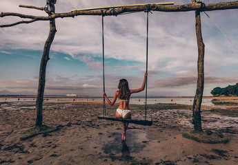 beautiful girl with dark hair in swimming suit posing in swing in ocean