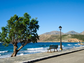 Bench with beautiful tree and lantern at a lonely sunny romantic beach on Crete, Greece