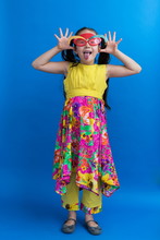  Adorable Asian Little Girl With Long Black Hair In Pig Tails And Colourful Summer Dress Standing Making A Face And Sticking Her Tongue Out While Wearing Party Elf Glasses