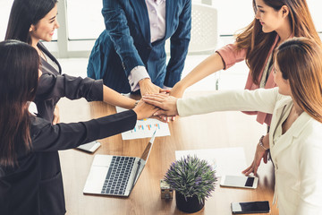 Businesswomen joining hands in group meeting at modern office room showing teamwork, support and unity in work and business. Female power and femininity concept.