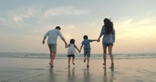 SLOW MOTION - Asian Family Running On The Beach At Sunset With Happy Emotion. Family, Holiday And Travel Concept. Back Rear View.
