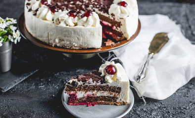 German, delicious Black Forest cake, with a delicate white cream, cherries in alcohol and dark chocolate on a dark stone table decorated with white linen fabric