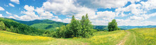 Beautiful Summer Countryside In Mountains. Wonderful Panoramic Scenery On A Sunny Day. Country Road Through Rural Fields. Hills And Mountains In The Distance. Blue Sky With Fluffy Clouds