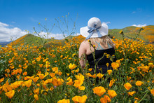 Young Woman Wearing Tank Top And Straw Hat Poses In Poppy Field, Looking Away