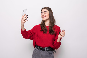 Portrait of a smiling cute woman in red sweater making selfie photo on smartphone isolated on a white background