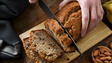 Wall Mural - Slicing banana bread. Hands slicing homemade banana bread with nuts on a cutting board