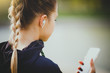 © Vasily Makarov - Young smiling girl making sport and running in the park using her phone to listen the music with wireless headphones on sunset in the city watching the screen