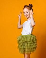 Portrait of a gorgeous red-haired girl looking at camera with a smile and showing peace sign with fingers