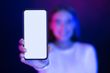 Girl showing blank smartphone screen over neon studio background