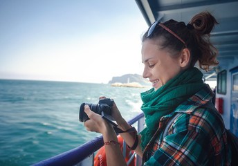 Young female traveler with a camera in her hands, on a ship against the sea, shoots a sea landscape