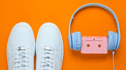 Wall Mural - Retro style. 80s. Pop culture. Minimalismalism. Headphones with audio cassette, white sneakers on orange background. Top view