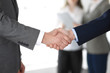 © rogerphoto - Business people shaking hands at meeting or negotiation, close-up. Group of unknown businessmen and women in modern office at background. Teamwork, partnership and handshake concept