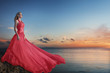 Beautiful young woman posing in luxurious long dress on the beach