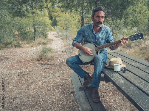 Fotomural attractive man with beard playing on banjo in the forest sitting at a table