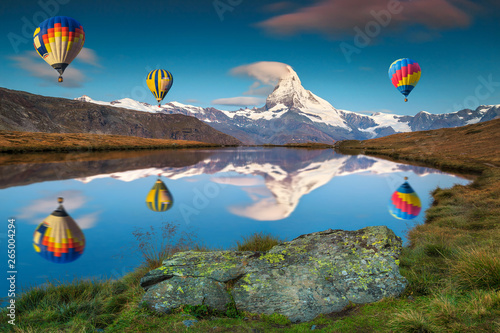 Leinwand Poster  Amazing Matterhorn peak and hot air balloons reflecting in water
