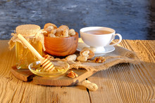 Honey Jar, Walnuts In A Wooden Cup, A Cup Of Tea On A Wooden Table In The Sunlight.