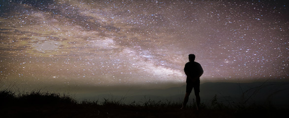 Wall Mural - colorful night sky with stars and silhouette of a standing man on the stone. blue milky way with man