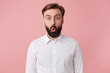 Photo of dazed handsome bearded man, didn't expect to hear the shocking news, wearing a white shirt. Looking at the camera with wide open mouth isolated over pink background.