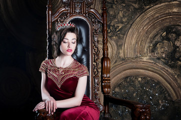 Queen in red dress sitting on throne. Symbol of power