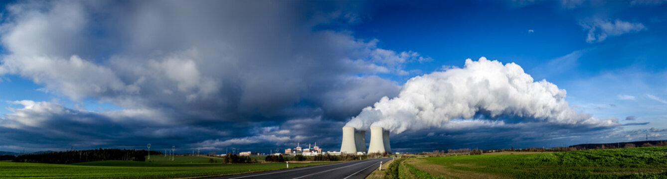 Nuclear plant and its cooling towers releasing a huge cloud of steam to the sky. Verdant vegetation around.