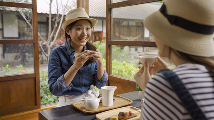 girl with surprised face holding tea bowl drinking hot tea in japanese local wooden house sitting on floor at table with dessert traditional sweets. young female travelers relaxing chatting indoor.