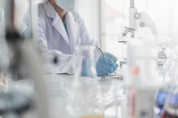 Wall Mural - a scientist hands writing on a clipboard in laboratory with test tube microscope and solutions.