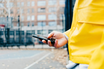 Wall Mural - Man in yellow raincoat using mobile phone while standing on the city street, close-up