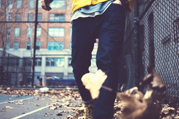 Wall Mural - Close-up of man's legs wearing jeans and yellow raincoat walking among fallen leaves in autumn