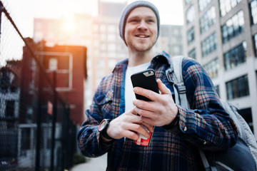 Wall Mural - Young happy man standing on the city street with mobile phone and cup of coffee and typing message