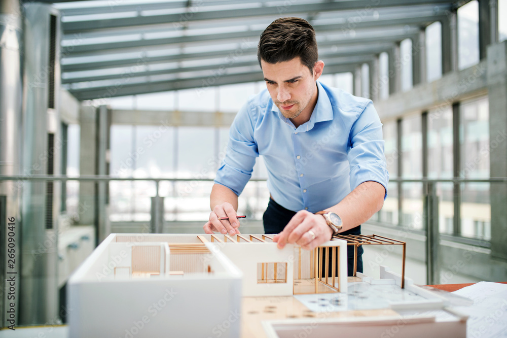 Young businessman or architect with model of a house standing in office, working. - obrazy, fototapety, plakaty 