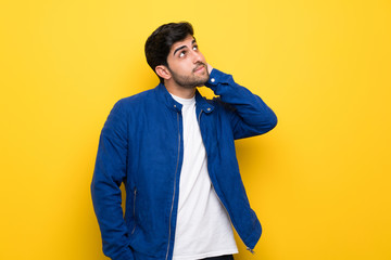 Man with blue jacket over yellow wall thinking an idea