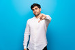 © luismolinero - Young man over isolated blue wall showing thumb down sign with negative expression
