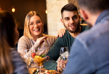 Wall Mural - Group of young friends having fun in restaurant, talking and laughing while dining at table.