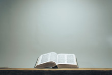 Open Holy Bible On A Old Oak Wooden Table.  Grey Wall Background..