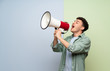 © luismolinero - Young man over blue and green background shouting through a megaphone