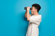 © luismolinero - Young man over blue background and looking in the distance with binoculars