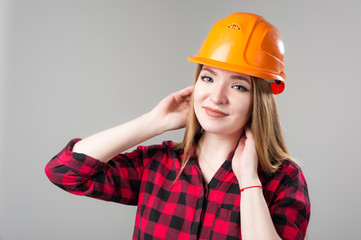 Portrait of a young attractive woman with blond hair in orange helmet on a neutral gray background.