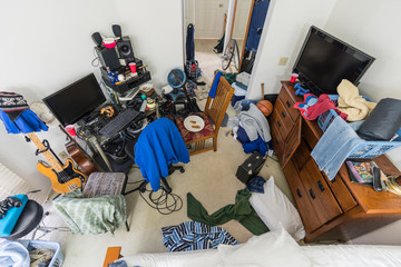 Very messy, cluttered suburban teenage boys bedroom with piles of clothes, music and sports equipment.  