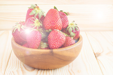 Strawberries in a bowl on a light wood background with place for text. Berry summer background.