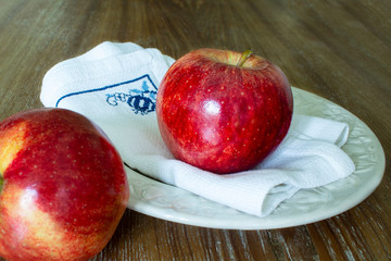 two red apples , one of them focused on white napkin of yarn on a wooden background