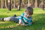 Fototapeta Dmuchawce - A little boy is smiling and lying on the green grass in the park.