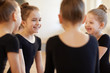 Group of cute girls giggling while sitting in circle during ballet class in studio lit by warm sunlight