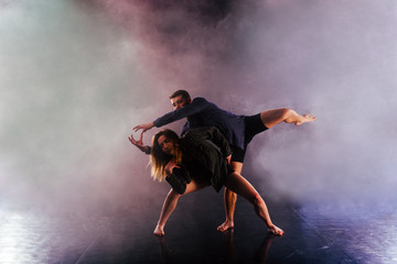 Wall Mural - Two modern dancers stretching their shoeless feet high in the air surrounded by smoke on stage.