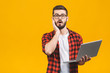 Portrait of amazed man holding laptop computer and looking at camera over yellow background.