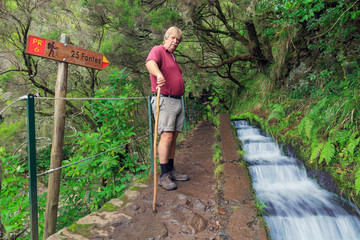 Canvas Print - Senior tourist hiking at the 25 Fontes falls, a cascade waterfall at the end of a levada hike on the island Madeira