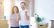 © Krakenimages.com - Middle age senior couple moving to a new home with boxes around smiling with happy face looking and pointing to the side with thumb up.
