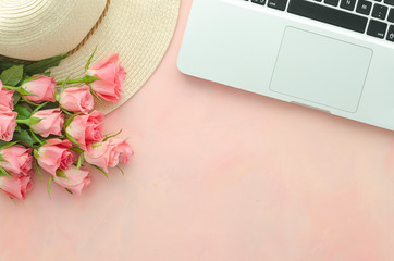 Women's workplace flat lay with pink roses on a pink background with a laptop and a straw hat. Copy space top view