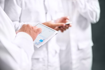 Employees confer stand in white coats using a tablet computer and telephone.